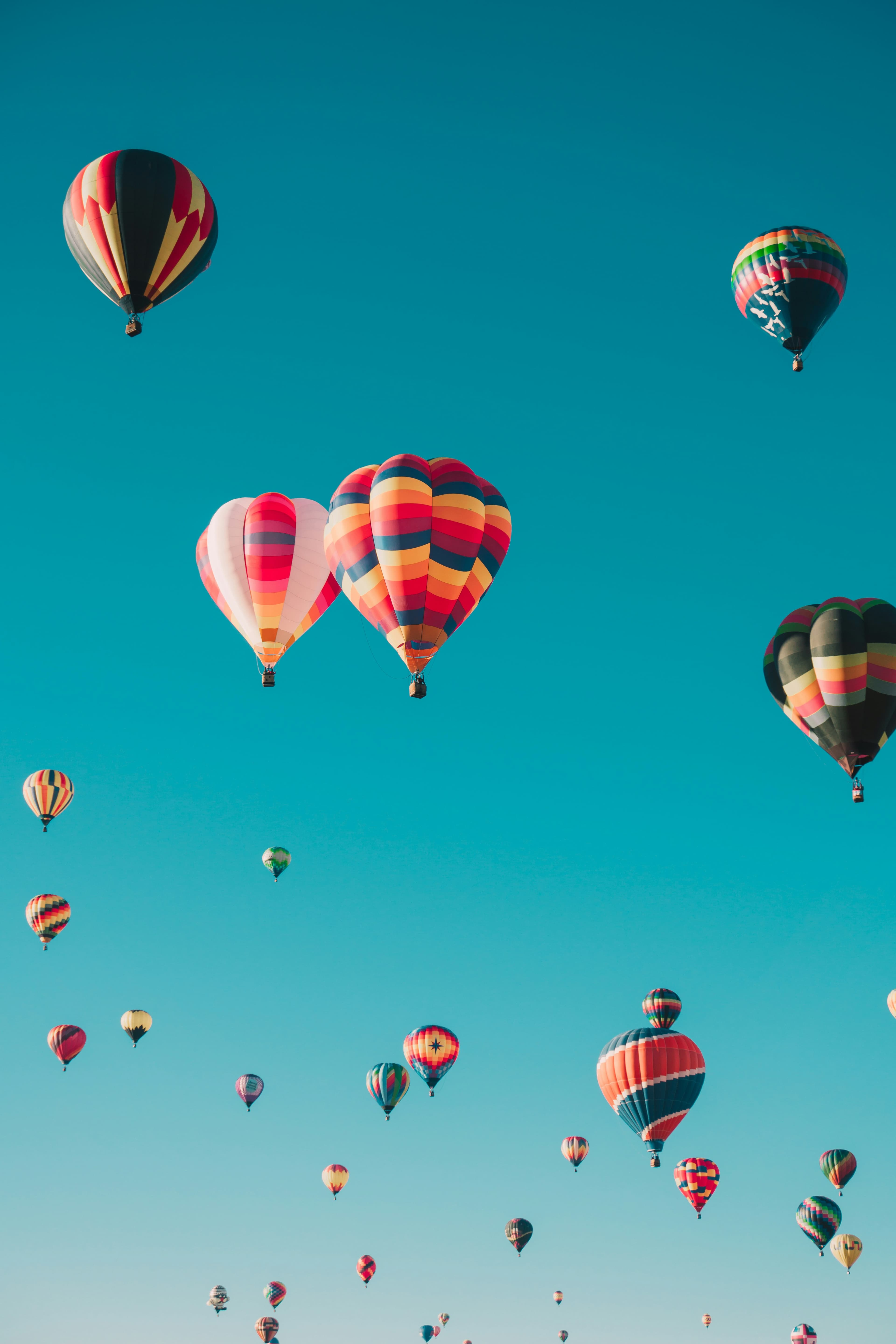 Dozens of colourful hot air balloons floating in a clear turquoise sky