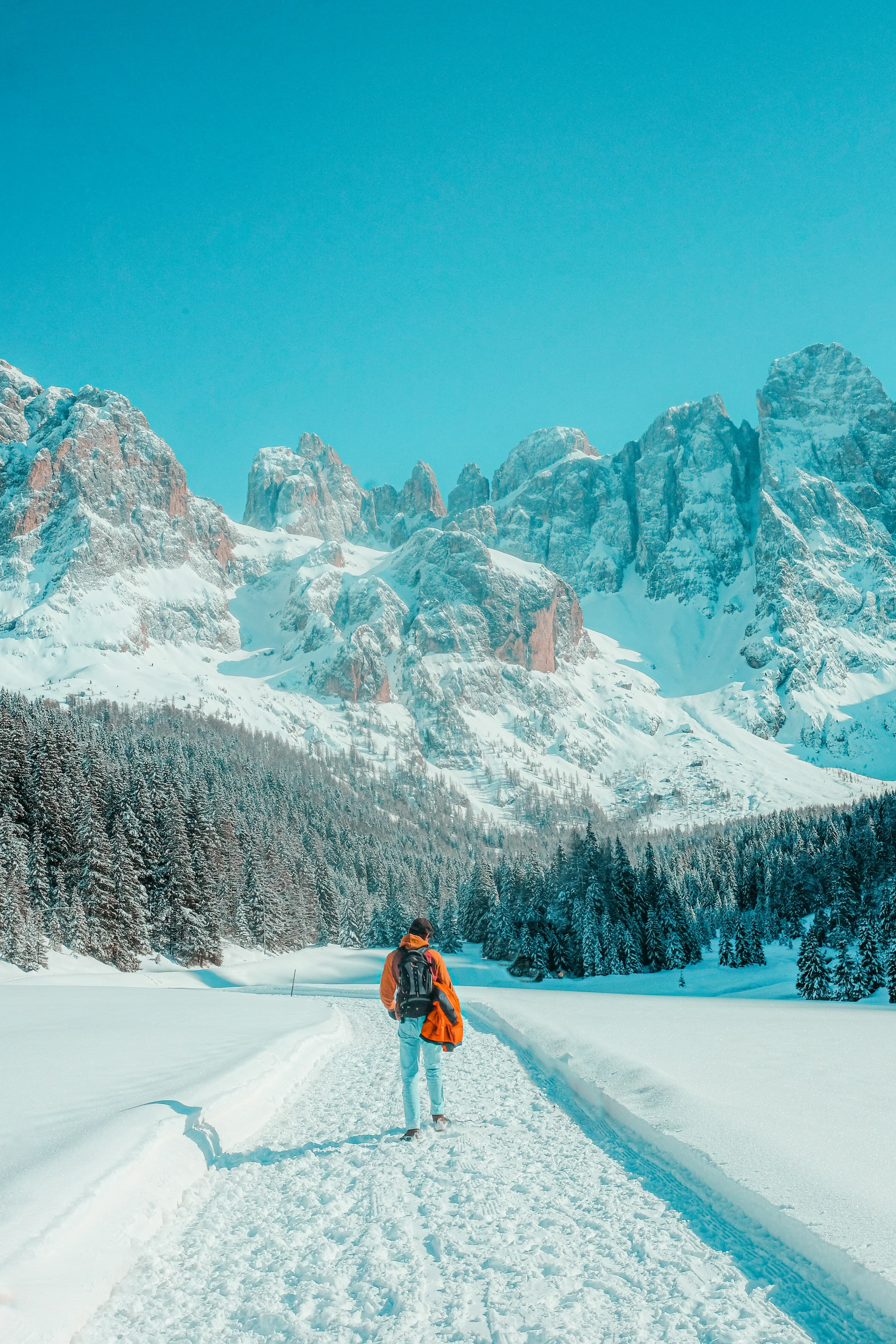 Hiker walking a snowy trail toward jagged alpine mountain peaks